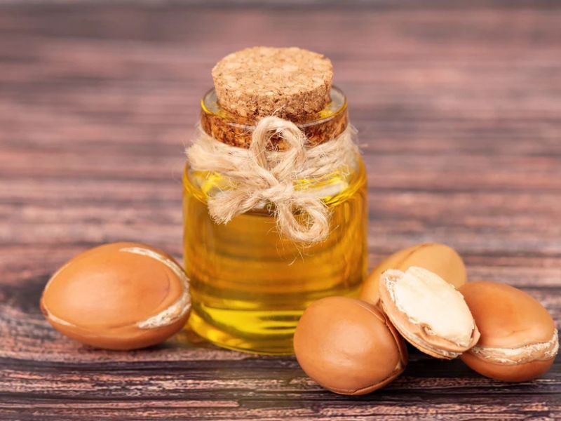 A bottle of Argan oil with a cork lid, surrounded by Argan nuts on a wooden surface.