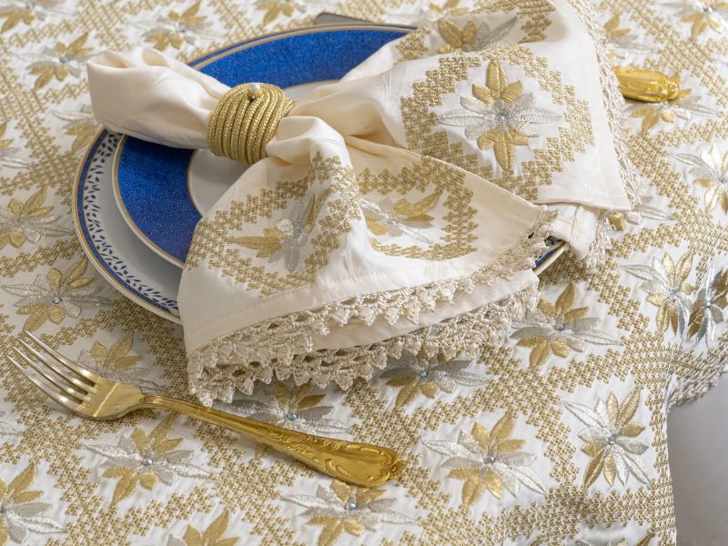 A beautifully set table featuring a plate with a bright blue edge, adorned with elegant Rabat embroidery napkins and a golden fork, showcasing the intricate textile art of Morocco.