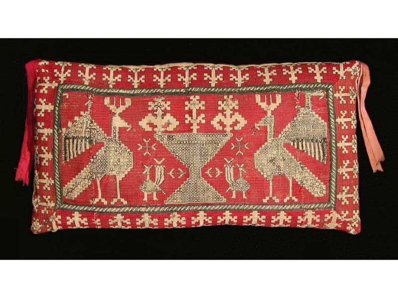 A handcrafted Azemmour embroidery cushion featuring intricate motifs of peacocks, floral designs, and geometric patterns on a vibrant red background.