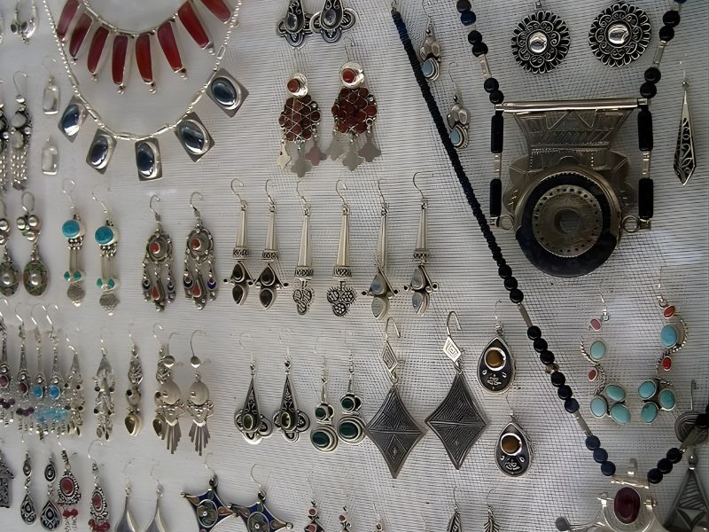A display of various traditional Moroccan jewelry pieces, including silver earrings, necklaces, and pendants, featuring intricate designs and colorful stones.
