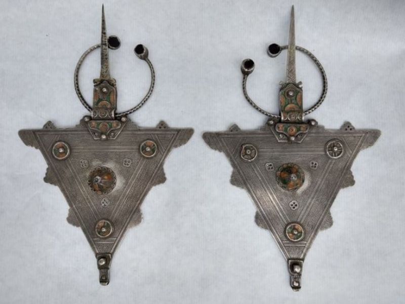 Amazigh Fibula brooch featuring intricate geometric patterns and decorative elements, made of silver and adorned with colored stones.