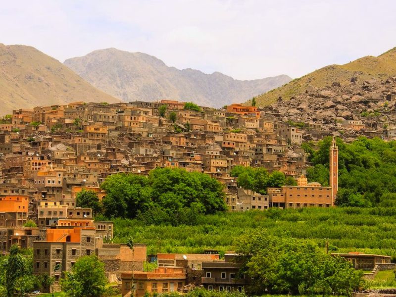 Aerial view of Imlil village in the Atlas Mountains, Morocco, featuring traditional Amazigh houses, greenery, and surrounding mountains.