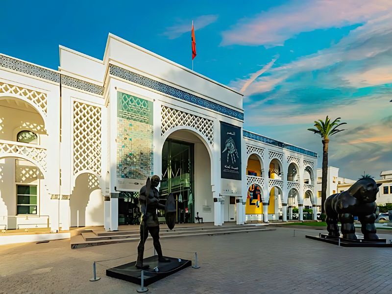Exterior view of the Mohammed VI Museum of Modern and Contemporary Art in Rabat, featuring striking architecture with double arches, a large entrance, and outdoor sculptures.