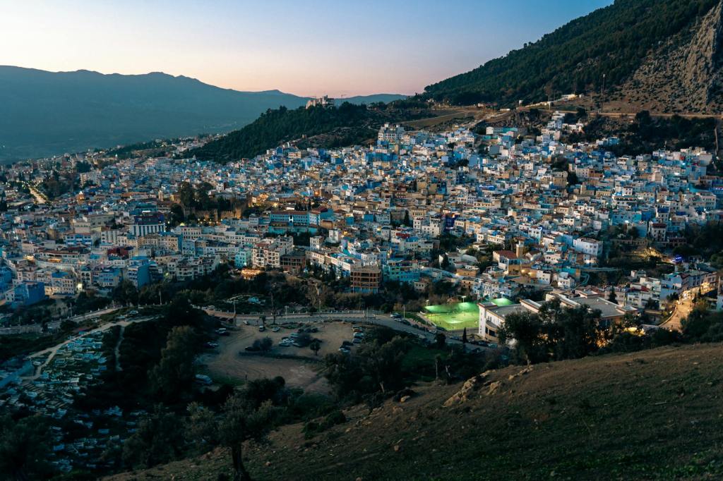 A panoramic view of Chefchaouen, the blue city in Morocco, nestled in the Rif Mountains, showcasing its stunning blue-painted buildings and surrounding natural landscape during twilight.
