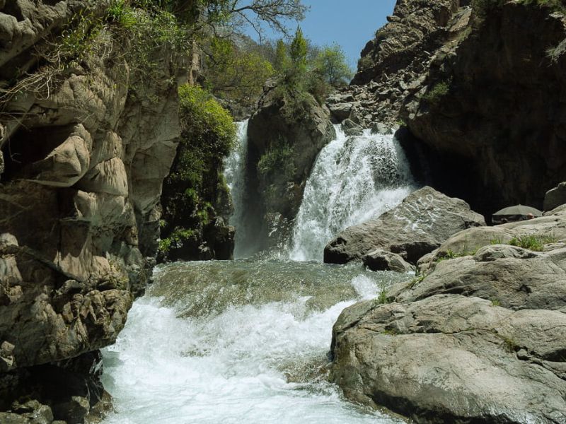 A scenic view of a waterfall cascading over rocky terrain in a lush green setting, surrounded by trees.