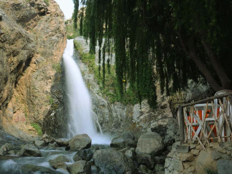 A breathtaking waterfall cascading down rocky cliffs in the Ourika Valley, surrounded by lush greenery and smooth stones.