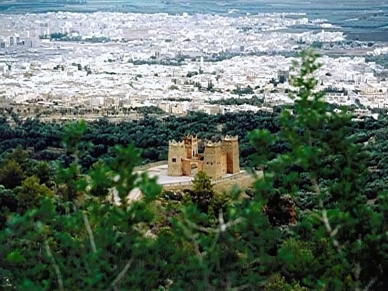 A scenic view of Beni Mellal, Morocco, showcasing a fortress surrounded by greenery with the city in the background.