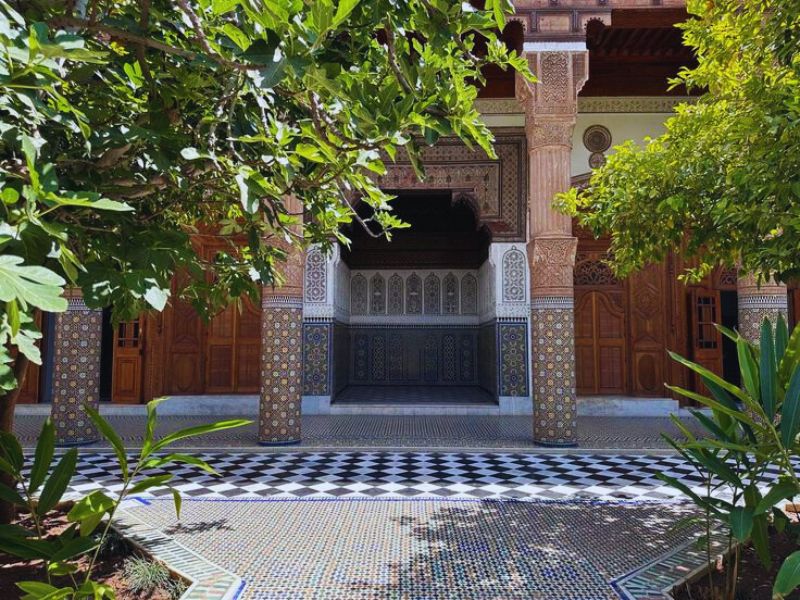 An ornate courtyard of Dar El Bacha, showcasing intricate Zellij tilework, lush greenery, and traditional Moroccan architectural features.