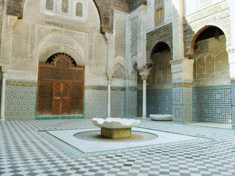 The tranquil courtyard of the Medersa al-Attarine in Fez, featuring intricate Zellij tilework, an elegant water basin, and ornate stucco detailing, showcasing the beauty of Marinid architecture.