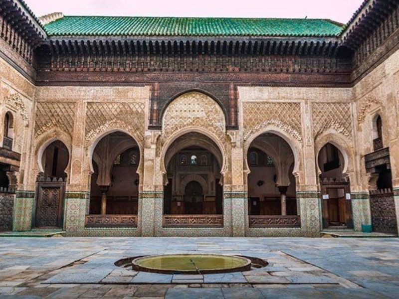 Interior view of the Medersa Bou Inania showcasing intricate arches, tilework, and central courtyard with a water basin.