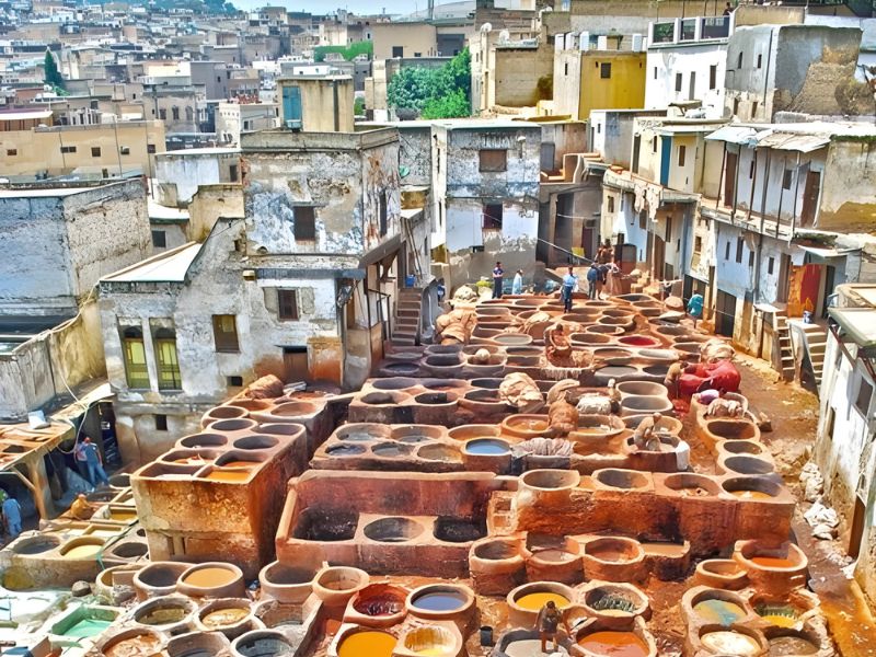 Aerial view of the Chouara Tannery in Fez, Morocco, showcasing numerous dyeing vats filled with colorful liquids and workers engaged in traditional leather processing.