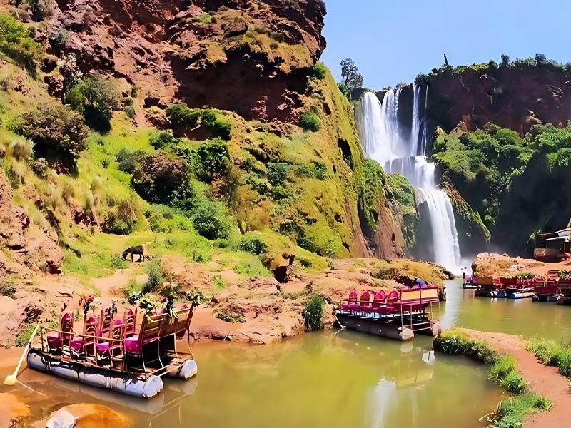 Scenic view of Ouzoud Waterfalls in Morocco, featuring cascading waterfalls surrounded by lush greenery, with a boat docked at the lake in the foreground.