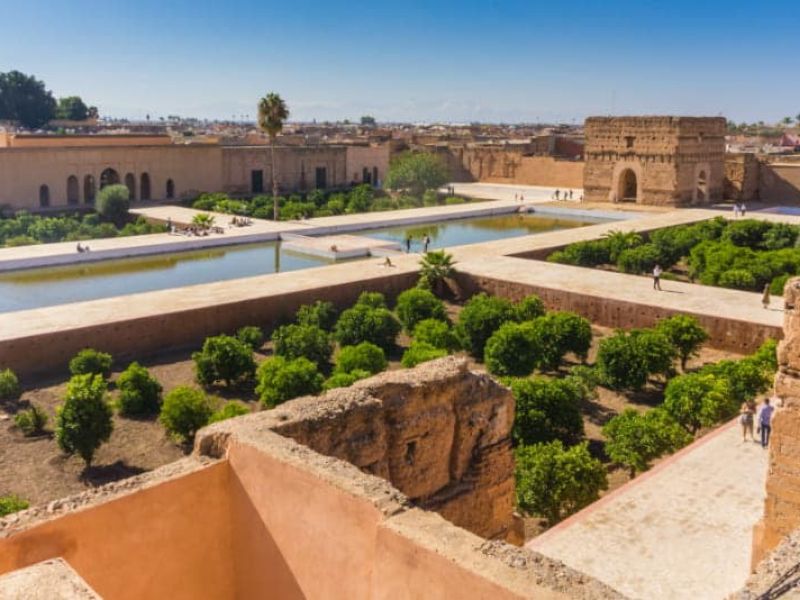 A panoramic view of the Badi Palace in Marrakesh, showcasing its beautiful gardens, symmetrical layout, and historical architecture with visitors exploring the grounds.