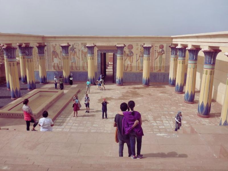 A scenic view of a film set resembling an ancient Egyptian temple, featuring colorful pillars and hieroglyphic decorations, with several people exploring the area.