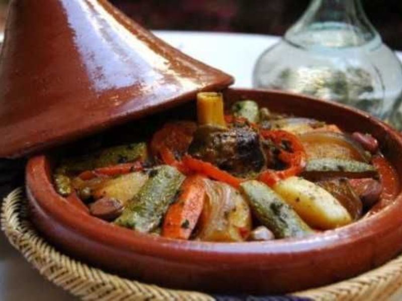 A traditional Moroccan tagine pot half-covered with a conical lid, filled with various vegetables and meat, showcasing the vibrant colors and textures of the dish.