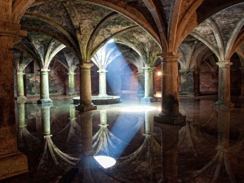 Interior of the Portuguese Cistern in El Jadida, Morocco, featuring Gothic columns and reflections on the water surface illuminated by light.