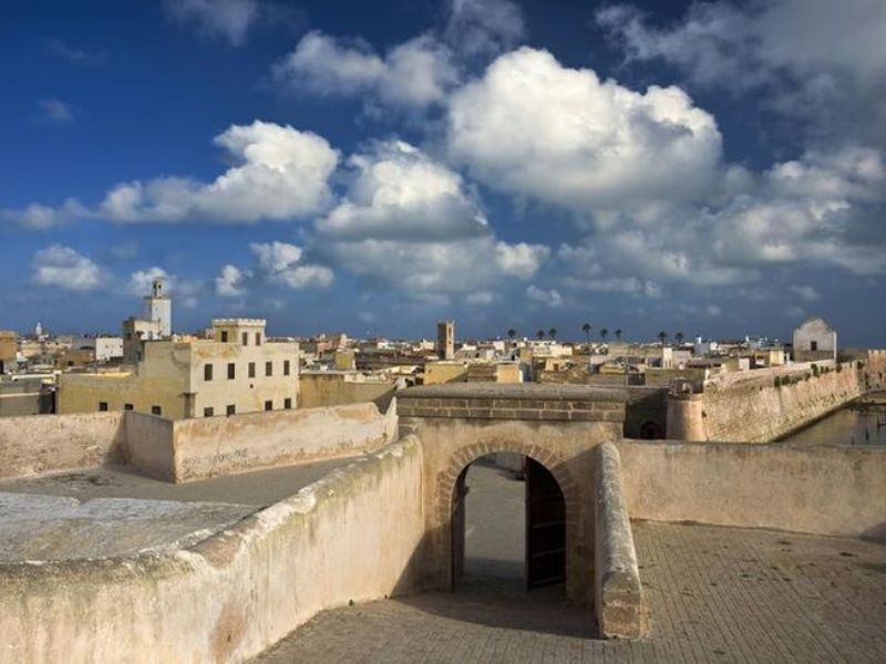 View of the fortified ramparts and rooftops of El Jadida, Morocco, under a blue sky with clouds.
