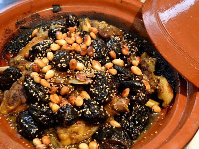A traditional Moroccan tagine dish featuring a mixture of succulent meat, dried fruits, and topped with toasted nuts, served in a signature earthenware pot.