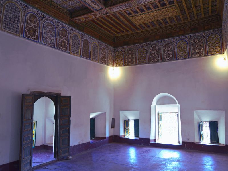 Interior view of a spacious room in Kasbah Taourirt, featuring intricate ceiling designs, arched doorways, and colorful windows.