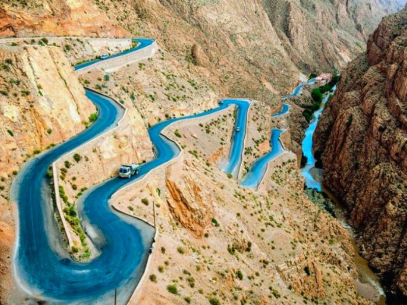 Aerial view of the winding road through the Dades Gorge in the High Atlas Mountains, showcasing dramatic cliffs and a river flowing below.