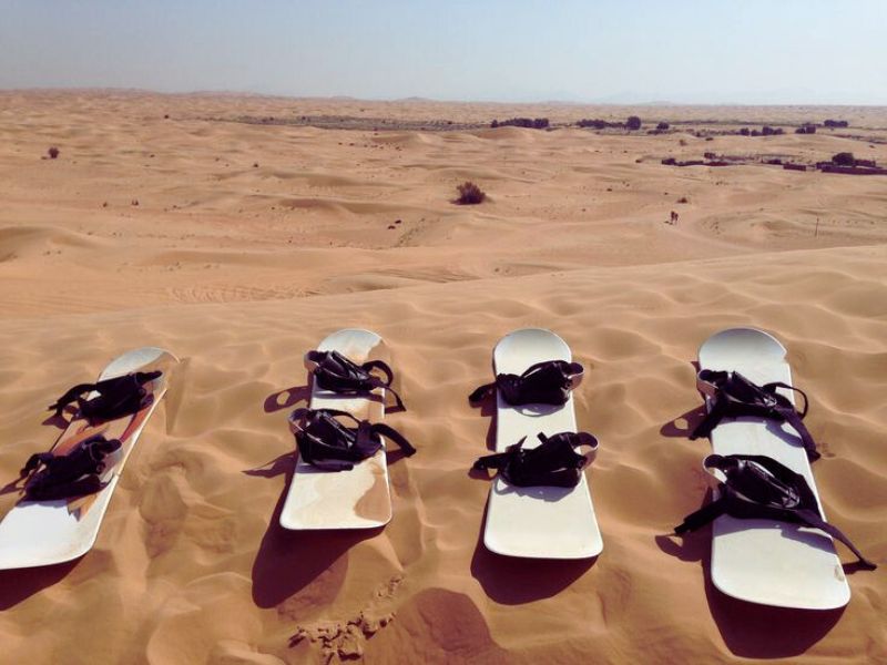 Four sandboards resting on golden dunes, with a vast desert landscape in the background.