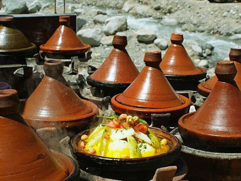 A selection of traditional Moroccan tagines cooking in a market, featuring conical clay pots with one pot displaying colorful vegetables and herbs.