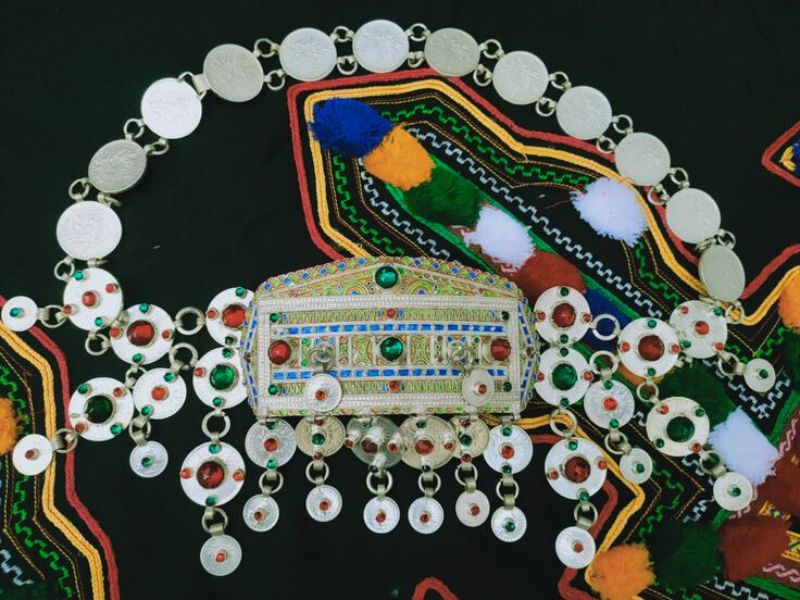 A beautifully crafted silver necklace adorned with colorful beads and intricate designs, set against a patterned background reflecting Amazigh culture.