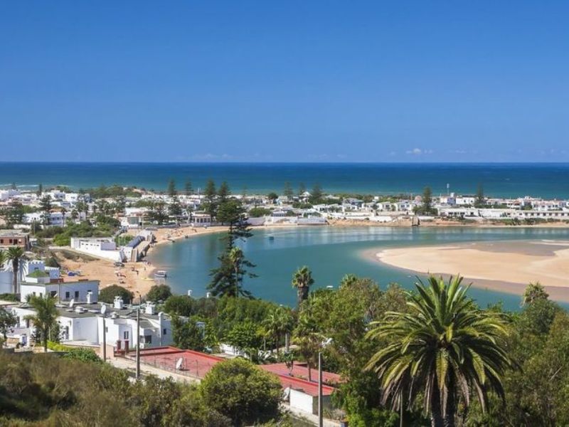 A scenic view of Walidia, Morocco, showcasing the tranquil lagoon, sandy beach, and white buildings along the coastline, with the Atlantic Ocean in the background.