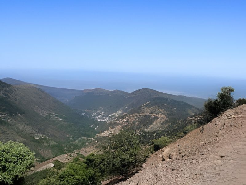 A panoramic view of the Beni Snassen Mountains in Morocco, showcasing rugged peaks, lush vegetation, and a distant village nestled in the valley.