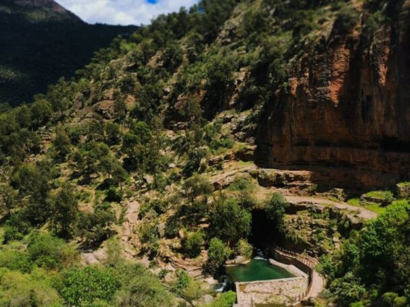 A scenic view of lush greenery and rocky cliffs in the Beni Snassen Mountains, featuring a natural pool and pathways.