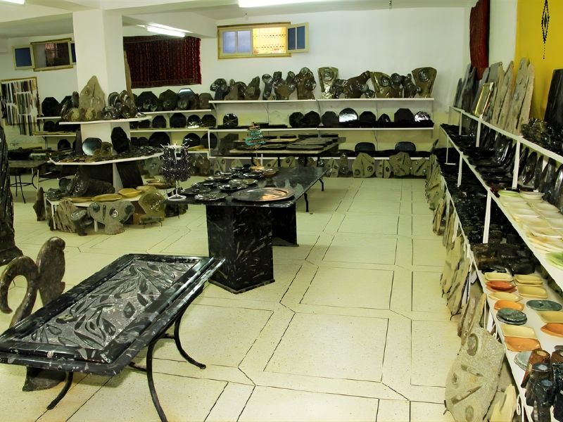 Interior of a fossil workshop in Erfoud, showcasing various fossilized marble and decorative items, including tables and plates, displayed on shelves.