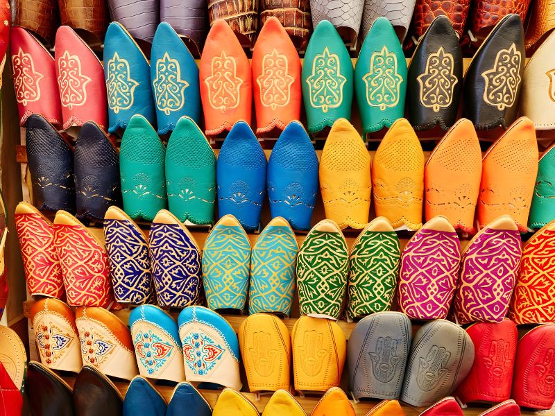 A display of colorful Moroccan Babouche slippers arranged in rows, showcasing various designs and vibrant hues, including pointed and rounded toes, highlighting traditional craftsmanship and cultural significance.
