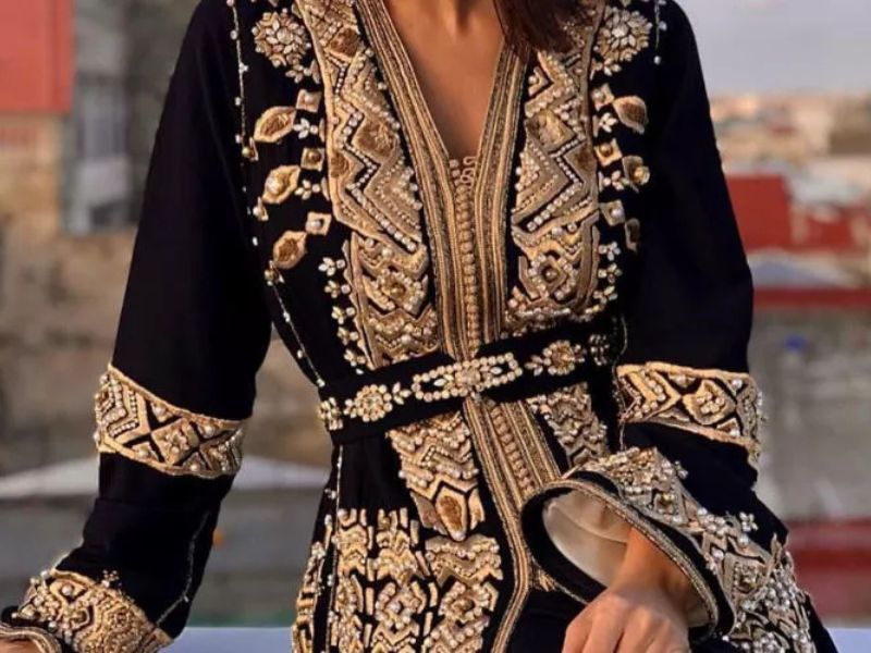 A woman wearing a luxurious black Caftan embellished with intricate gold embroidery, showcasing Moroccan craftsmanship.