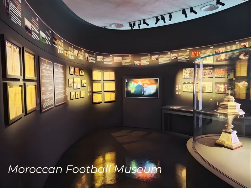 Interior view of the Moroccan Football Museum, featuring display panels, photographs, and a trophy under glass.