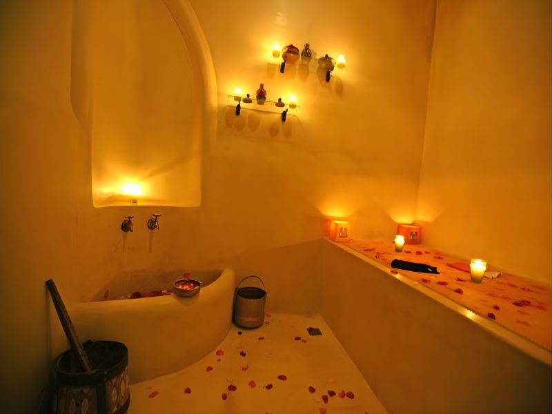 A serene interior of a traditional Moroccan Hammam, featuring soft lighting, candles, and rose petals scattered on the benches, creating a tranquil atmosphere for relaxation and cleansing.