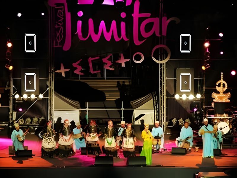 A group of musicians performing on stage at the Timitar Festival in Agadir, showcasing traditional Amazigh culture alongside vibrant lighting and festival branding.