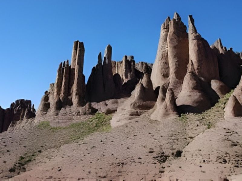 Rock formations rising sharply against a clear blue sky, with varying shapes and heights on a sandy landscape.