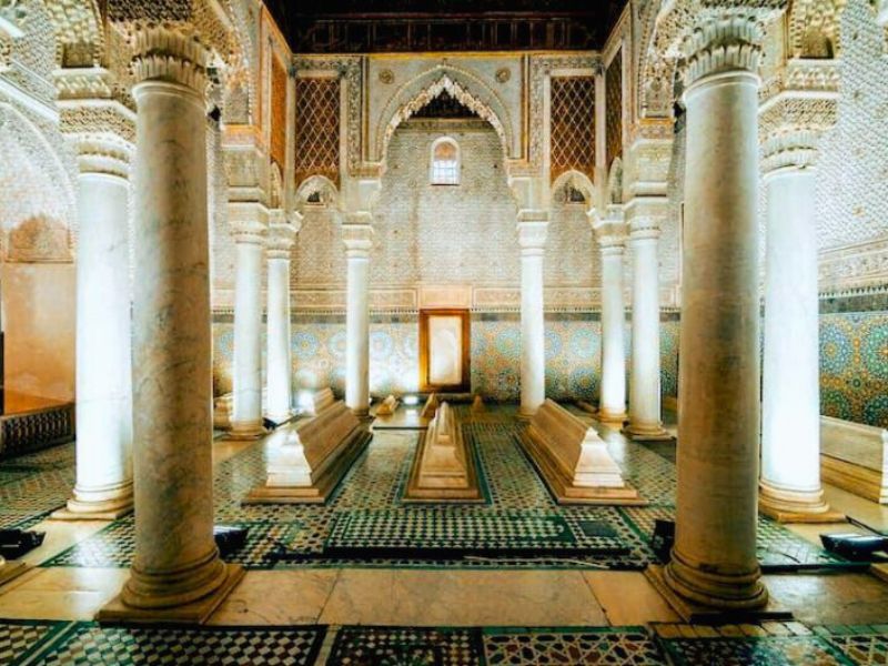 Interior view of a historical building featuring marble columns, intricate tilework, and three ornate tombs in a large, well-lit space.