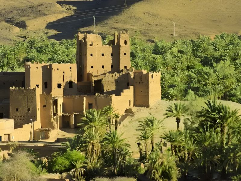 An ancient adobe building surrounded by lush palm trees in a desert landscape.