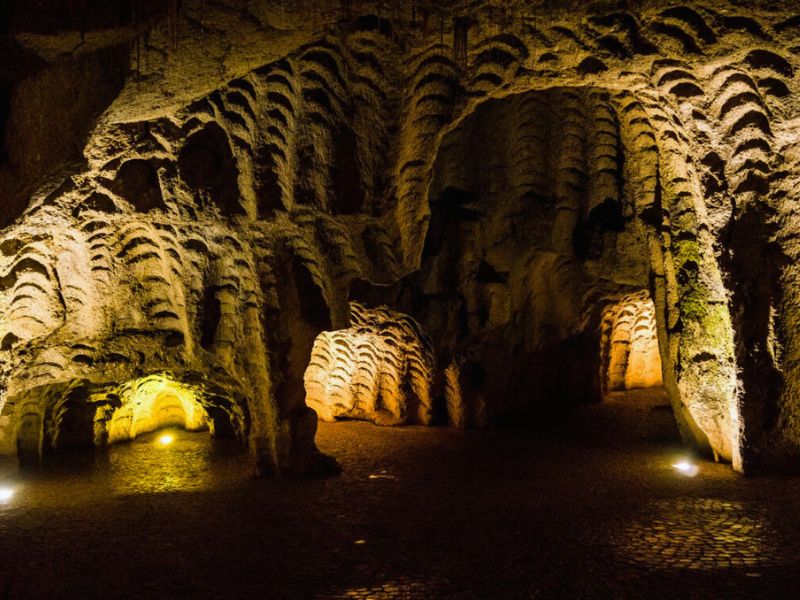 Interior view of a cave with textured rock formations and soft yellow lights illuminating the path.
