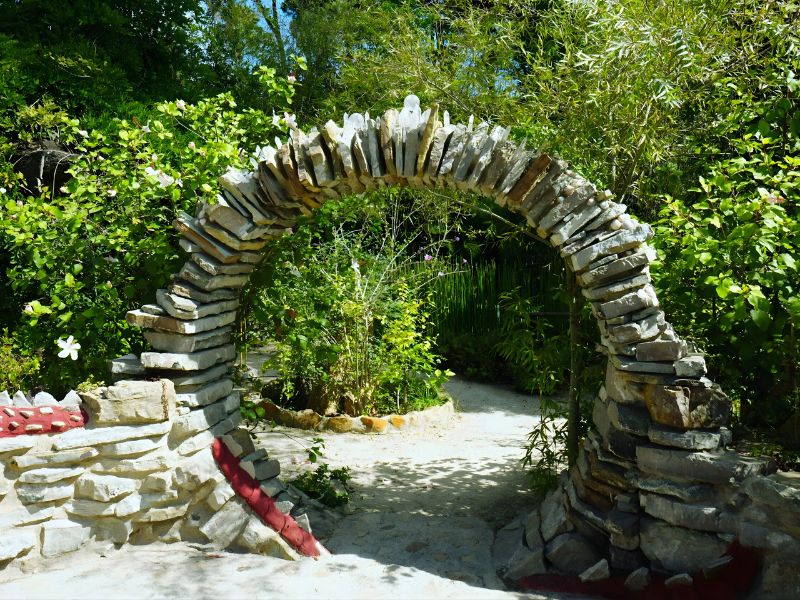 A stone archway surrounded by lush greenery and colorful flowers, leading into a garden path.