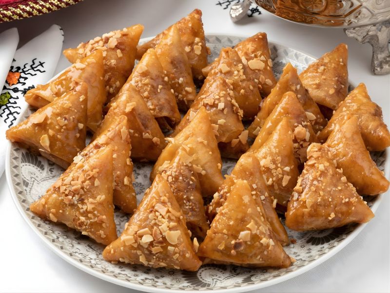 A plate of golden-brown samosas topped with chopped nuts, displayed on an ornate platter.