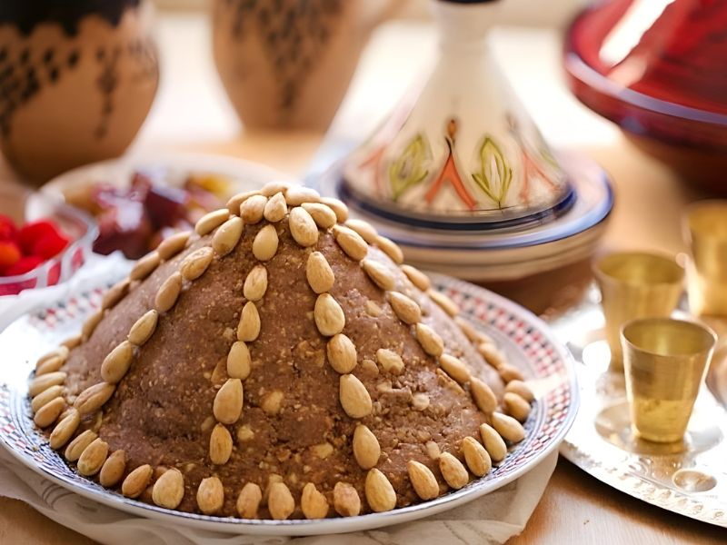 A beautifully presented traditional dessert shaped like a dome, topped with almonds and surrounded by decorative Moroccan pottery and brass cups.