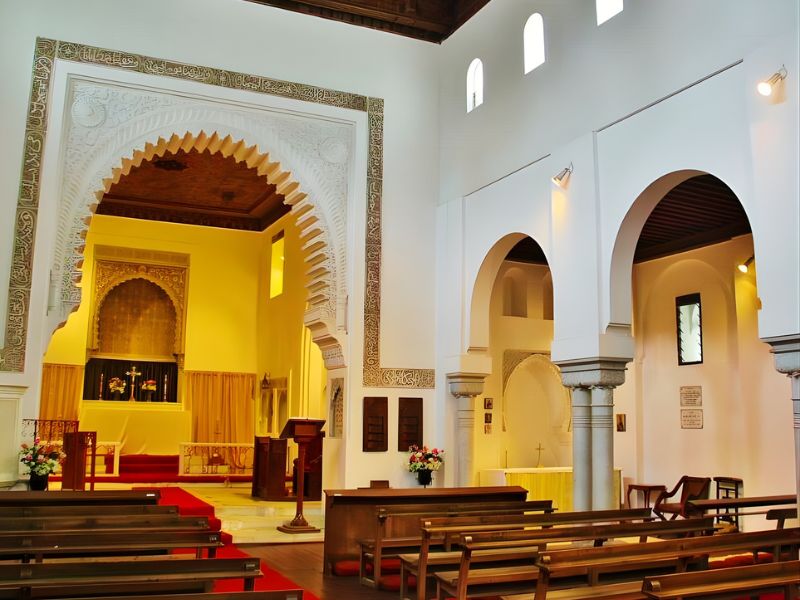 Interior view of a religious building featuring ornate archways, wooden ceilings, and rows of wooden benches.