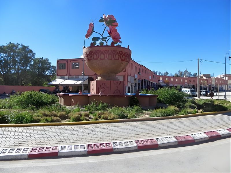 A large pink flower sculpture in a decorative bowl within a city roundabout.