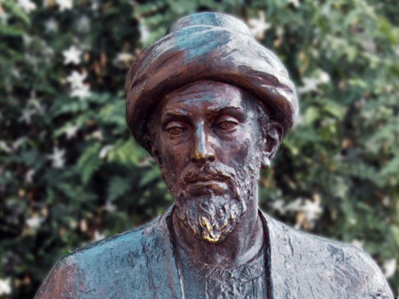Bronze statue of a man wearing a turban and traditional clothing with a blurred green leafy background