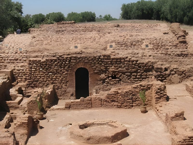 Ancient stone and brick ruins with archways and a circular stone structure in the foreground under a clear sky