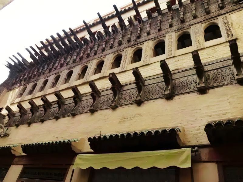 Close-up of an intricately carved wooden balcony with decorative brackets and ornamental designs on a yellowish wall