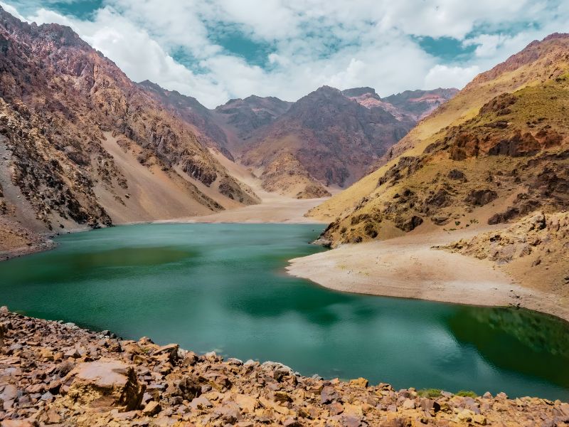 A turquoise lake surrounded by steep, rocky mountains under a partly cloudy sky
